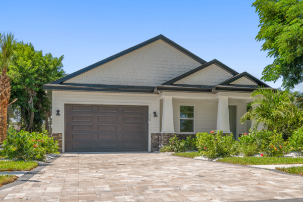 Front view of a suburban house with a double garage door, white siding, and a landscaped front yard under a clear blue sky.