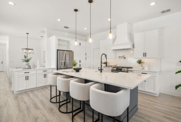 Bright white kitchen with a large island, pendant lights, and stainless steel fridge.