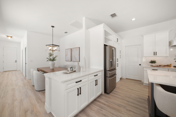Bright white kitchen with a large island, white cabinets, stainless steel refrigerator, and light wood flooring. Open-concept kitchen featuring marble countertops, pendant light over the island, and a potted plant on the counter.