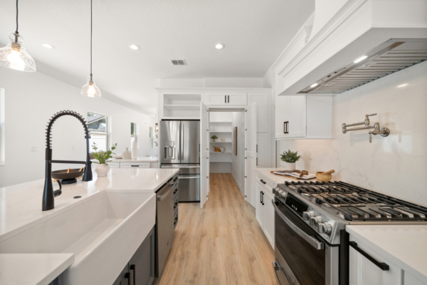 Bright, modern kitchen with white cabinets, wood floor, and stainless steel appliances; large island with black faucet and pendant lights.