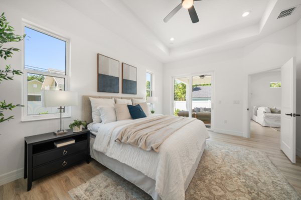 Bright contemporary bedroom with a beige bed, matching bedding, black nightstands, and large windows letting in natural light.
