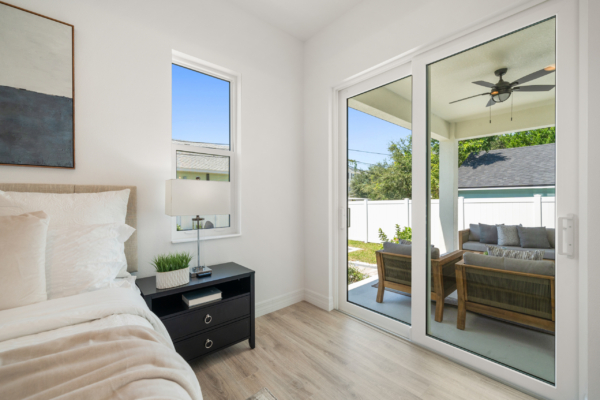 Bright bedroom with white walls, a black nightstand, and a large sliding glass door opening to a patio.