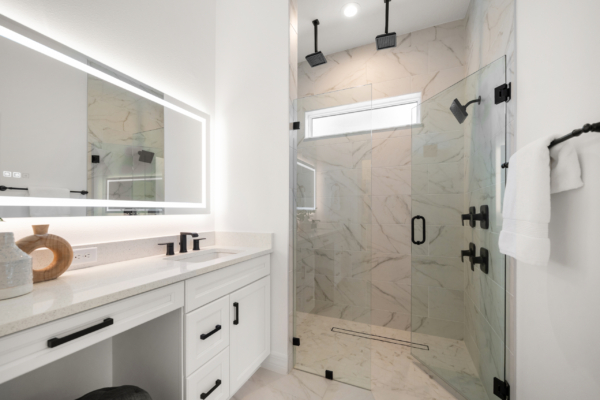 Bright, modern bathroom with white cabinetry and a marble-tiled shower, featuring a glass enclosure and two ceiling rainfall showerheads with black fixtures.