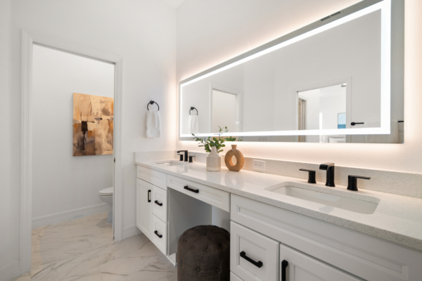 Modern bathroom with a long backlit rectangular mirror above a double vanity, white cabinetry, and a marble floor.