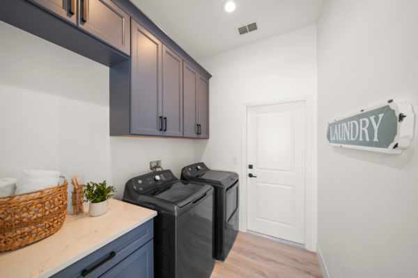 Laundry room with blue cabinets, white countertop, and stacked front-loading washer and dryer beneath a sign reading LAUNDRY.
